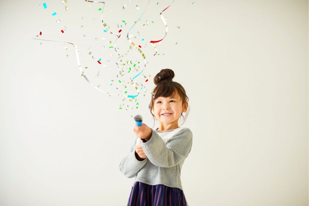 a little girl is shooting confetti into the air in celebration with a big smile 