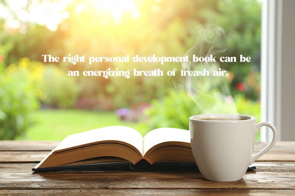 a book and a steaming mug are in front of a sunny window with text overlay that reads "The right personal development book can be an energizing breath of fresh air."