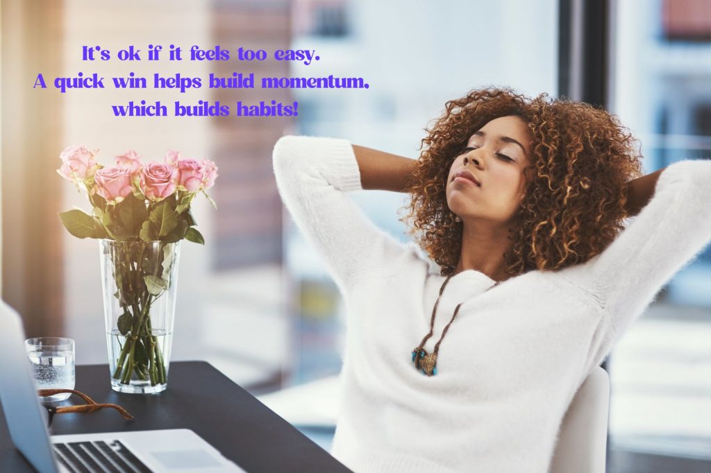 a woman is leaning back, relaxed in her chair in front od a laptop and flowers. Text reads "It’s ok if it feels too easy. A quick win helps build momentum, 
which builds habits!"