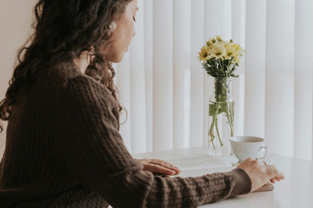 woman seated at table with flowers and tea cup reading and reflecting 