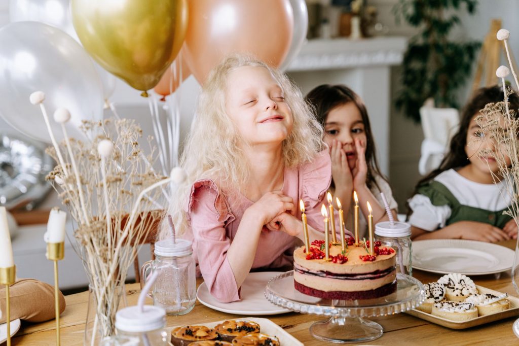 little girl making a wish over beautiful birthday cake with candles at a birthday party 