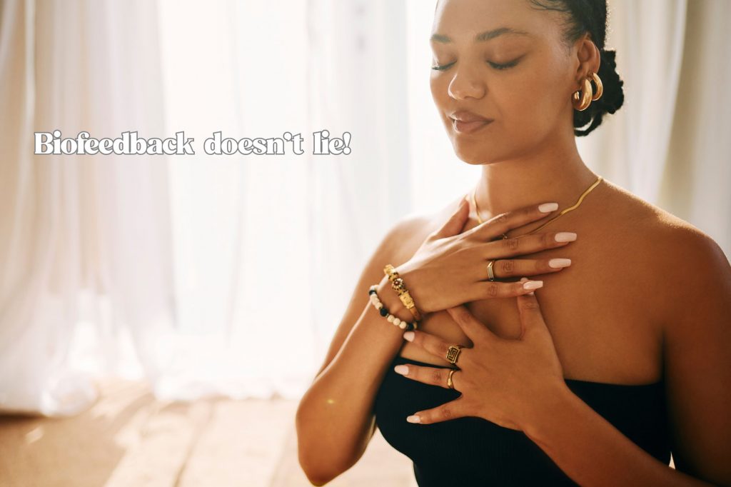 A woman is breathing with hands on chest and pleasant face in a sunny room with text overlay that reads "biofeedback deosn't lie!" 