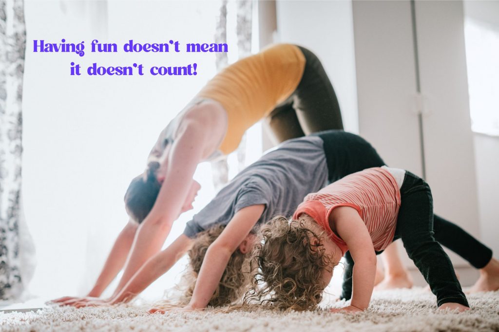 A woman and two children do a cute, imperfect downward facing dog yoga pose in a line on a fuzzy rug 
