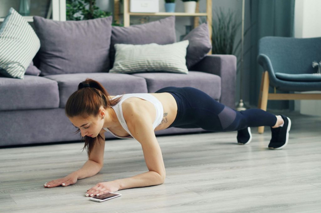 a woman does a plank in her living room with a phone next to her 