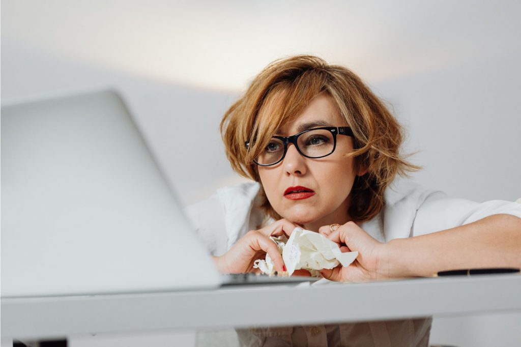 Overwhelmed woman looking at a computer with messy hair and crumpled paper in her hands 