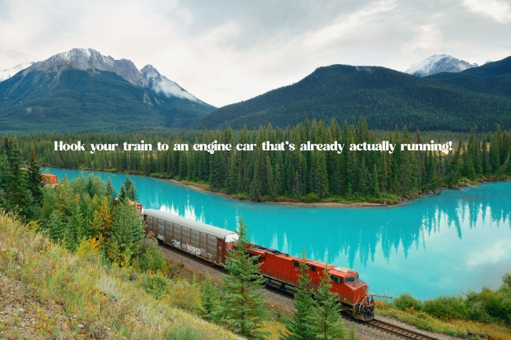 A train drives through the forest in front of mountains and a beautiful lake with text overlay that reads "Hook your train to an engine car that’s already actually running!"