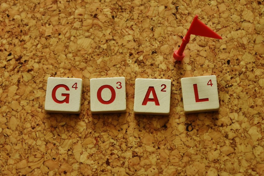 a cork board with "GOAL" in scrabble letters and a red flag pin like a target 
