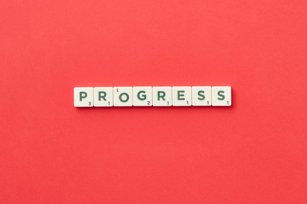 red background and the word "progress" in scrabble tiles 