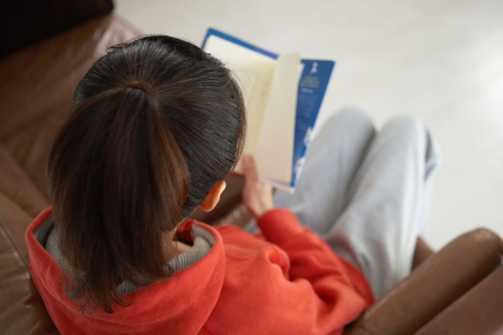 a girl is reading on a couch in sweatpants